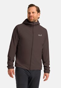 Veste à capuche marron avec une fermeture éclair intégrale, des poignets élastiques et un logo sur la poitrine ; conçue avec un matériau lisse et léger.