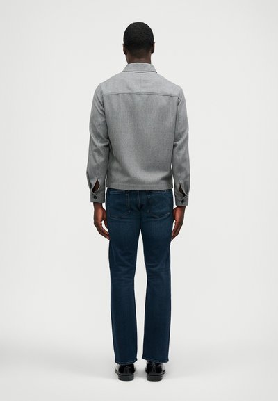 Pelēks austs žakets ar apkakli, garām piedurknēm un sānu šķēlumiem, kopā ar tumši zilām džinsiem. Audumam ir smalka tekstūra.