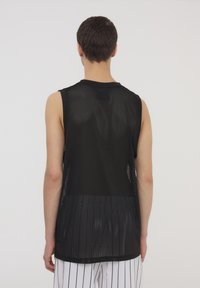 Canottiera sportiva nera senza maniche con un design traspirante e una vestibilità ampia. La parte posteriore mostra un evidente motivo in rete nera e pantaloni corti a righe.