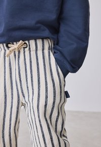 Gestreepte pyjamabroek in wit en marineblauw, met een trekkoord in de taille, een zachte textuur en een label met "BAKER" op de zijnnaad.