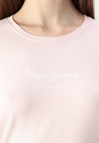Rózsaszín pamut póló, kerek nyakkivágással. Az elején egy fehér, írott betűs "Pepe Jeans LONDON" felirat látható.