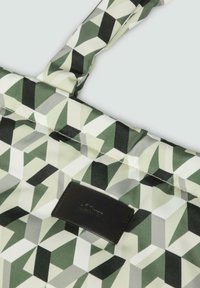 Geometrisch patroon stof tas in groen en zwart, met een gestructureerd zwart label. Het ontwerp bevat driehoeken en rechthoeken in verschillende tinten.