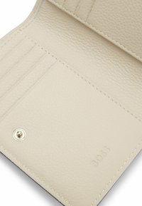 Wnętrze portfela z jasnobeżowej skóry, z przegródkami na karty, teksturowaną powierzchnią i srebrnym zatrzaskiem. Widać wytłoczone logo.