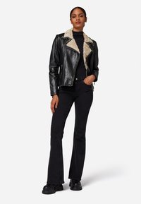 Zwarte leren motorjack met een beige nep-fur kraag, gecombineerd met zwarte flared jeans en chunky zwarte laarzen. Eenvoudig, casual ontwerp.