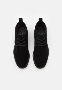 Botas de tobillo de ante negro con una textura suave, puntera redondeada, diseño con cordones y una lengüeta en el talón para ponerlas fácilmente.