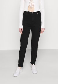 Los jeans de mezclilla negros presentan un corte ajustado, un diseño clásico de cinco bolsillos y acentos metálicos. Combinados con zapatillas blancas y una parte superior de canalé.