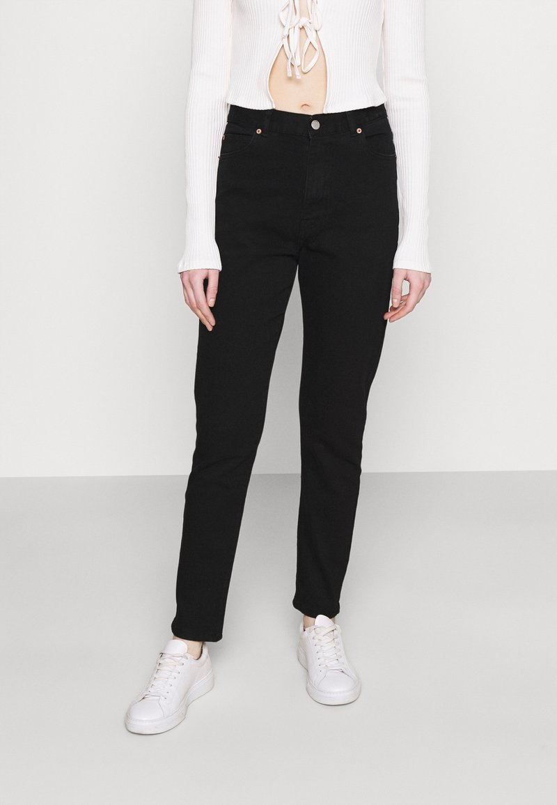Los jeans de mezclilla negros presentan un corte ajustado, un diseño clásico de cinco bolsillos y acentos metálicos. Combinados con zapatillas blancas y una parte superior de canalé.