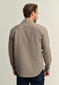 Braun, texturiertes Hemd mit spitzem Kragen, langen Ärmeln und Knopfmanschetten; verfügt über einen abgerundeten Saum und schlichte Stickdetails.