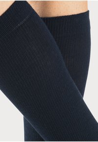 Jūras spēku tumši zilas ceļgala augstuma zeķes ar ribota tekstūra, kurām ir gluda augšējā josla un viegla auduma sastāvs, kas piemērots ikdienas valkāšanai.