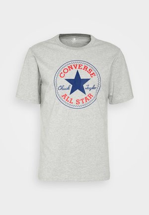 Camiseta de algodón gris con un gráfico circular que presenta una estrella azul, texto rojo que dice "CONVERSE ALL STAR" y "Chuck Taylor", y un borde de costura.