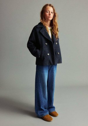Marineblauer, doppelreihiger Strickmantel mit entspannter Passform; kombiniert mit hellblauen weit geschnittenen Jeans und braunen Wildleder-Slippern.