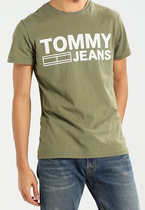 Oliwkowo zielony bawełniany T-shirt z dużym białym napisem "TOMMY JEANS" na piersi. Klasyczny okrągły dekolt i krótkie rękawy.