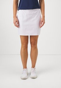 Jupe blanche midi avec une texture lisse et une taille �élastique, associée à des chaussures de sport blanches. Design minimal, adapté à la tenue de sport.