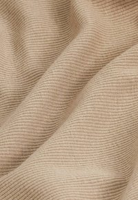 Gros plan sur un tissu côtelé beige montrant un tricot doux et texturé avec des plis délicats et des lignes horizontales.