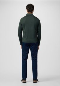 Dunkelgrünes langärmliges Hemd, marineblaue Hose, schwarze Sneakers. Hat ein schlichtes Design ohne sichtbare Muster oder Logos und zeigt einen lässigen Stil.