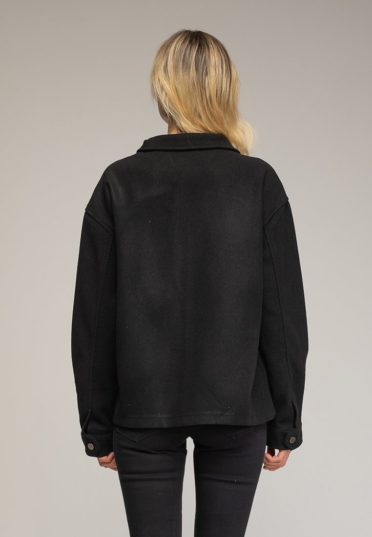 Camisa chaqueta negra oversize con cuello, mangas largas y cierres de botones, confeccionada en una tela texturizada y con un dobladillo recto.