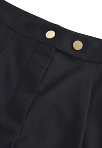 Pantalon noir à taille ajustée, avec deux boutons dorés et des plis discrets, fabriqué en tissu lisse à finition mate.