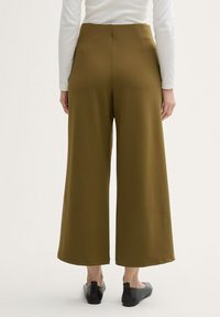 High-waisted, wide-leg trousers in olive green fabric, featuring a smooth texture and two back pockets, paired with black flat shoes.