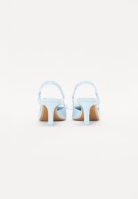 Svetlo modre sandale na peto z gladko površino, s slingback trakcem in ozko peto. Rjava podloga z minimalnimi oblikovalskimi detajli.