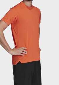 Kortærmet atletisk T-shirt i stærk orange, lavet af letvægtsmateriale med en glat tekstur. Har en rund hals og sideskår.