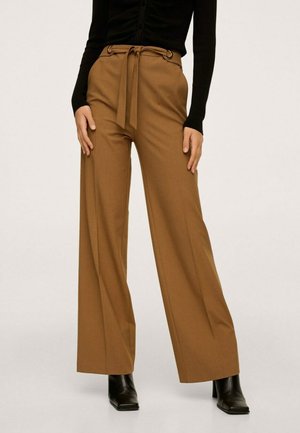 Femme portant un pantalon marron taille haute à jambes larges avec une ceinture en tissu et des bottines noires à talons, associé à un haut noir.