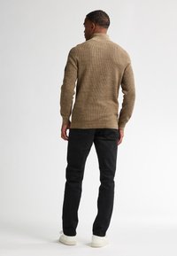 Neule, ruskea, korkean kauluksen omaava paita, jossa on teksturoitu muotoilu, yhdistetty mustiin farkkuihin ja valkoisiin lenkkareihin. Yksinkertainen, rento ilme takaa.