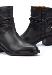 Botas de cuero negras hasta el tobillo con un diseño arrugado, punta afilada, tacón bajo en bloque y herrajes decorativos en el lateral. Textura suave y acabado elegante.
