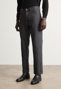 Jeans noirs taille haute à jambe droite en denim. Avec une poche avant et une fermeture à bouton, ils présentent une finition texturée subtile.