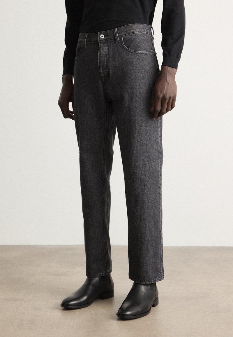 Jeans noirs taille haute à jambe droite en denim. Avec une poche avant et une fermeture à bouton, ils présentent une finition texturée subtile.