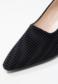 Chaussure pointue en tissu noir avec une texture côtelée, une doublure intérieure lisse et une silhouette flexible. Design de la semelle non visible dans cette vue.