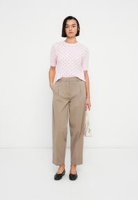 Ροζ ελαφρύ πλεκτό πουλόβερ με κοντά μανίκια και ανοιχτό σχέδιο, σε συνδυασμό με μπεζ παντελόνι ψηλόμεσο, φαρδύ στο κάτω μέρος, και μαύρες μπαλαρίνες.