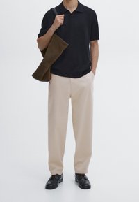 Lyhythihainen musta poolopaita, beiget housut ja tummat kengät; pitää kädessään ruskeaa mokkanahkaista olkalaukkua. Yksinkertainen muotoilu, sileä pinta.