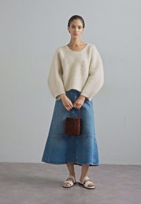Lys beige, pelsete strikkegenser med bred utringning; blå denimskjørt med flagrende nederkant; liten brun teksturert håndveske; hvite sandaler.