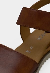 Καφέ δερμάτινο σανδάλι με δύο φαρδιές λουρίδες και επενδεδυμένο πάτο. Διαθέτει ραφές και υφασμένη μπεζ σόλα. Μέγεθος G 4½.