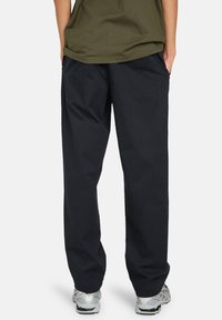 Pantalons en coton noir à coupe décontractée, dotés de poches latérales et d'une texture lisse, associés à des baskets grises.