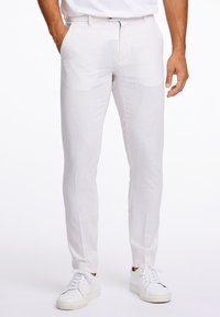 Bílé lněné kalhoty s úzkým střihem, rovný přední díl, boční kapsy a jemná textura, doplněné bílými teniskami.