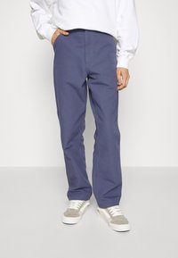 Pantalones de mezcla de algodón azul con diseño de pierna recta, que cuentan con cremallera y bolsillos frontales, combinados con zapatillas gris y blancas.