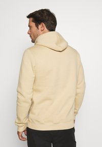 Beige hoodie met een grote, ronde capuchon, ribgebreide manchetten en zoom. Heeft een gestructureerde stof en een achteraanzicht, dat een relaxte pasvorm toont.