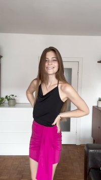 Černý bezrukávový top s rolákem, zkombinovaný s růžovou mini sukní s nařasením. Hladký povrch, přiléhavý design a živý kontrast barev.