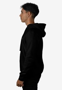 Sudadera con capucha negra vista de perfil, con textura de tela lisa y puños acanalados, con un logo pequeño en el frente.