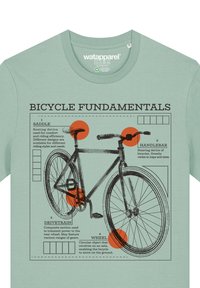 T-shirt vert menthe avec un diagramme de vélo comportant des parties étiquetées : selle, guidon, système de transmission et roue, mises en valeur par des cercles oranges.