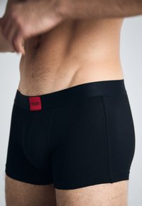 Schwarze Boxershorts aus weichem Stoff, mit einem glatten Bund und einem roten "HUGO"-Logo. Enganliegendes Design, mittlere Oberschenkellänge.