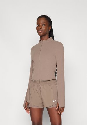 Haut à manches longues zippé marron associé à un short à taille élastique assorti. Les deux sont fabriqués dans un matériau doux et comportent un petit logo Nike blanc.