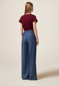 T-shirt corte corto bordeaux a maniche corte e pantaloni in denim a gamba larga, caratterizzati da una texture liscia e una vita alta, con un design minimalista.