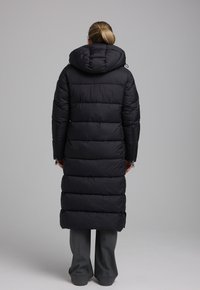 Zwarte pufferjas met een capuchon, voorzien van een lange, iets taps toelopende ontwerpen, horizontale stiksels en zijritsen voor een verstelbare pasvorm.