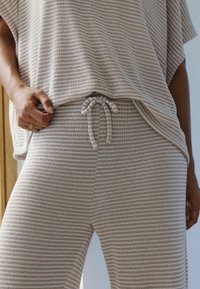 Light beige loungewear set featuring a striped short-sleeve top and drawstring pants, made from soft, textured fabric.