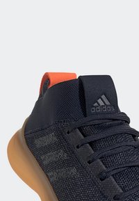 Scarpa da ginnastica in rete blu navy con linguetta arancione e suola in gomma. Presenta dettagli testurizzati e un accento con il marchio sulla linguetta.