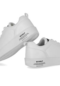Hvide sneakers med en glat syntetisk overdel, flad gummisål og sort branding på hælen. Inkluderer en bagside træksløjfe for nem påtagning.