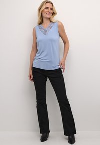 Haut sans manches bleu clair avec des détails en dentelle au col en V, associé à un pantalon noir évasé et des bottes noires à talons.