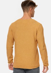 Long-sleeve sweater in mustard yellow knit fabric. Features a textured surface, round neckline, and slightly curved hem at the back.